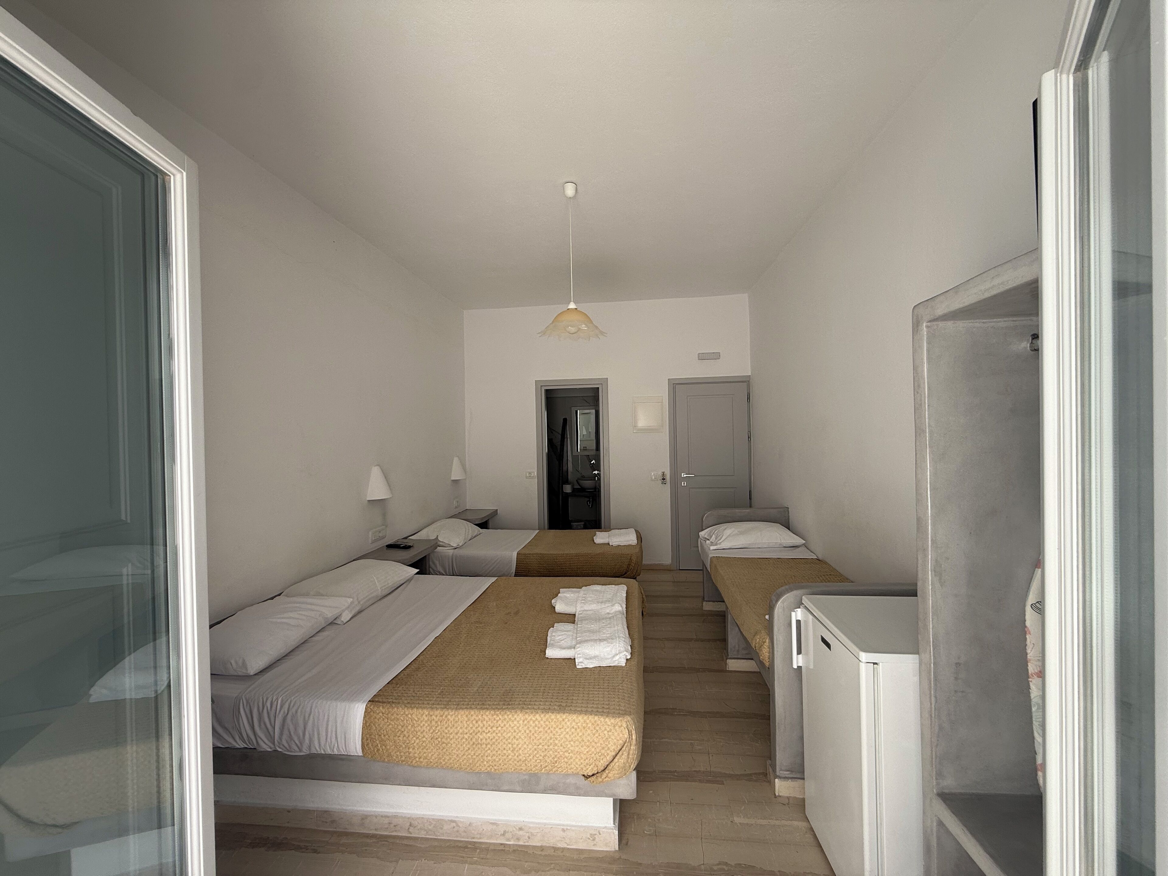 Een compacte hotelkamer met twee enkele bedden, een kleine kitchenette en een deur naar een badkamer.
