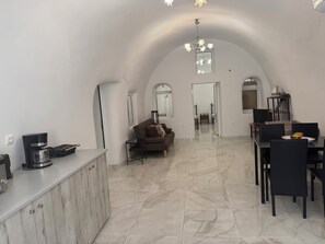 Amplia sala de estar con techo alto, estación de café, mesa de comedor con sillas y sofá.