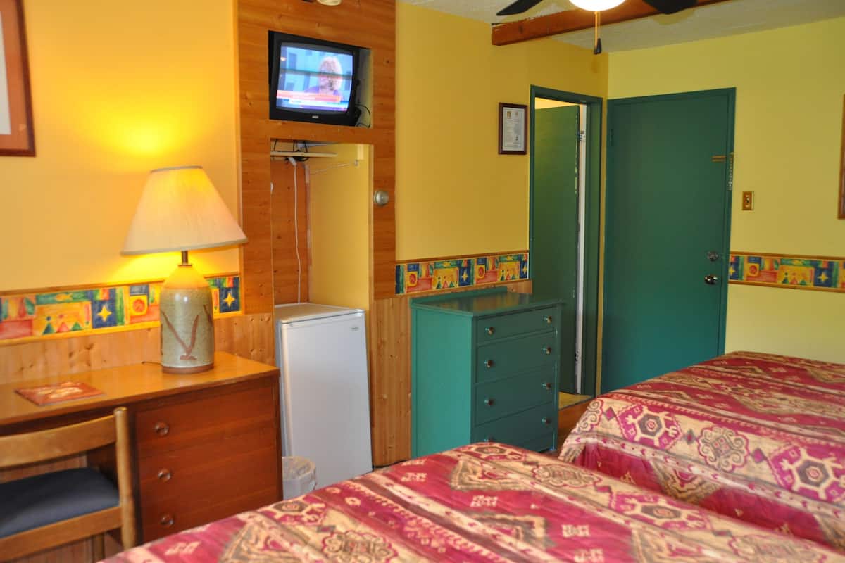 Una habitación con una cama, un escritorio con lámpara, televisor y refrigerador.