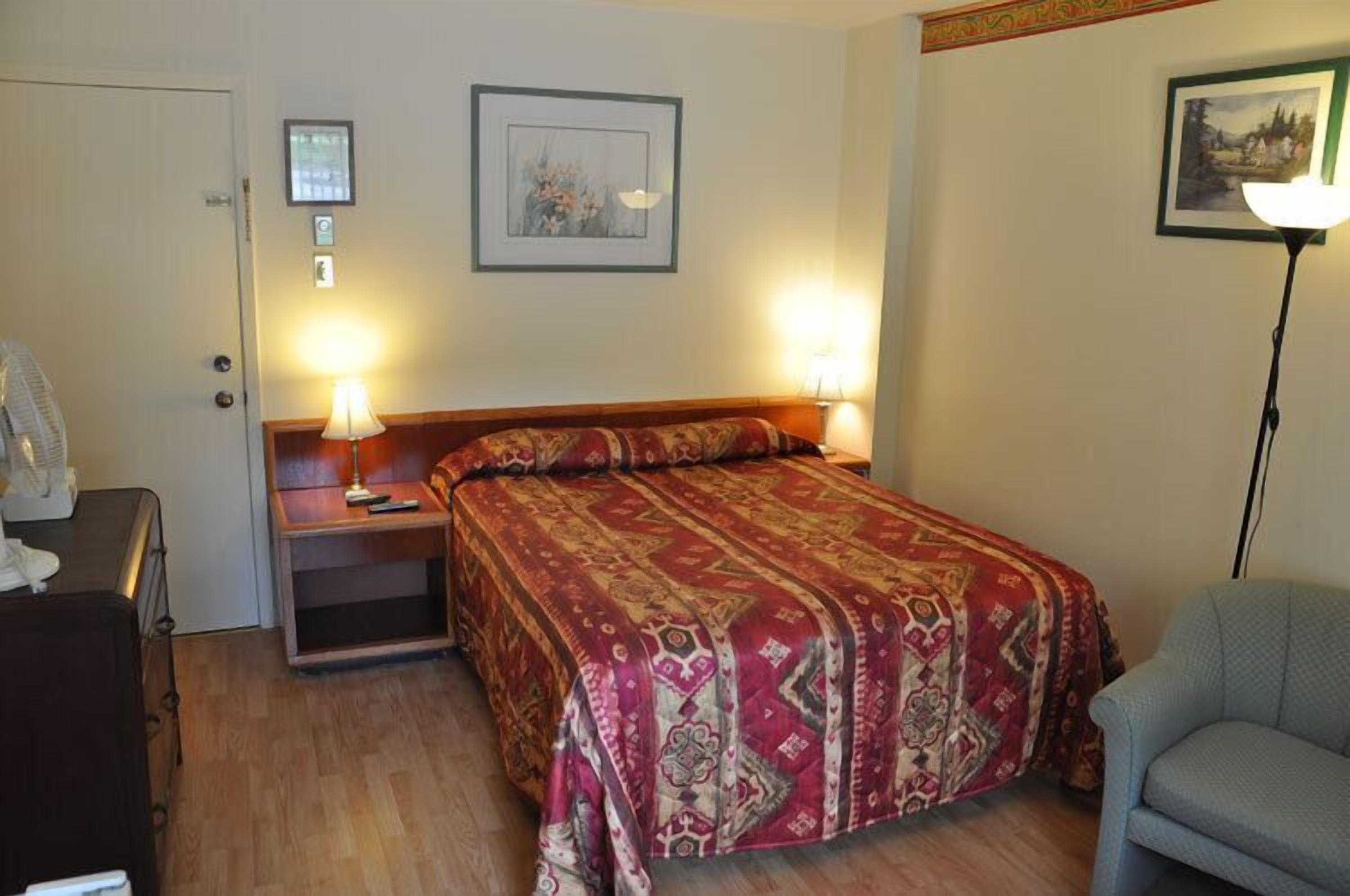 A hotel room with a bed, bedside tables, a lamp, a chair, and a door.