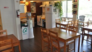 Un espace repas avec des tables et des chaises en bois, un réfrigérateur, une machine à café et une poubelle de recyclage.