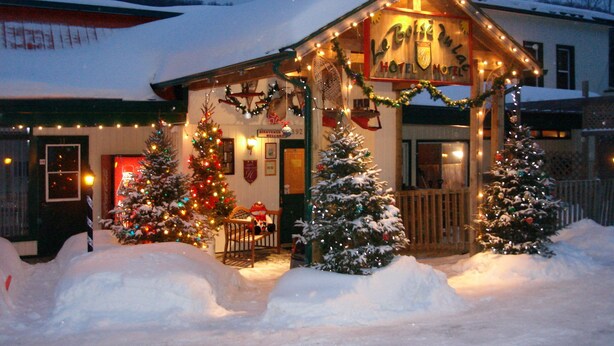 Un hôtel dont le toit est recouvert de neige et qui est décoré pour Noël, avec notamment un sapin et des guirlandes lumineuses.