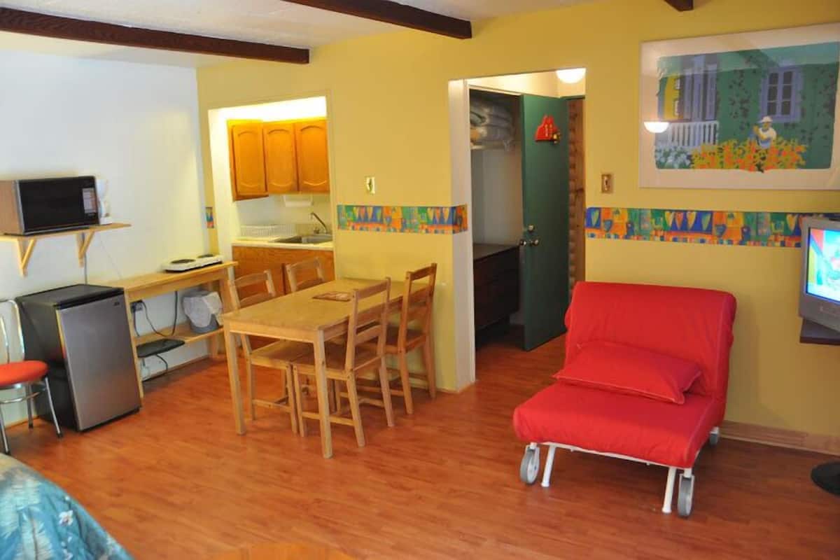 Un espacio habitable compacto con comedor, kitchenette y una silla roja.
