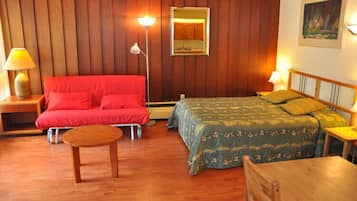 A room with two beds, a wooden floor, a red sofa, a small round table, and a mirror on the wall.