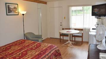 Une chambre d’hôtel équipée d’un lit, d’un bureau, d’une chaise, d’une table, d’un téléviseur et d’une fenêtre avec des stores.