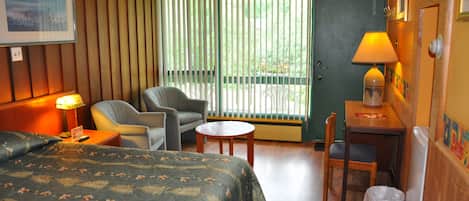 A hotel room with a bed, a chair, a small table, a lamp, and a door leading to a balcony.