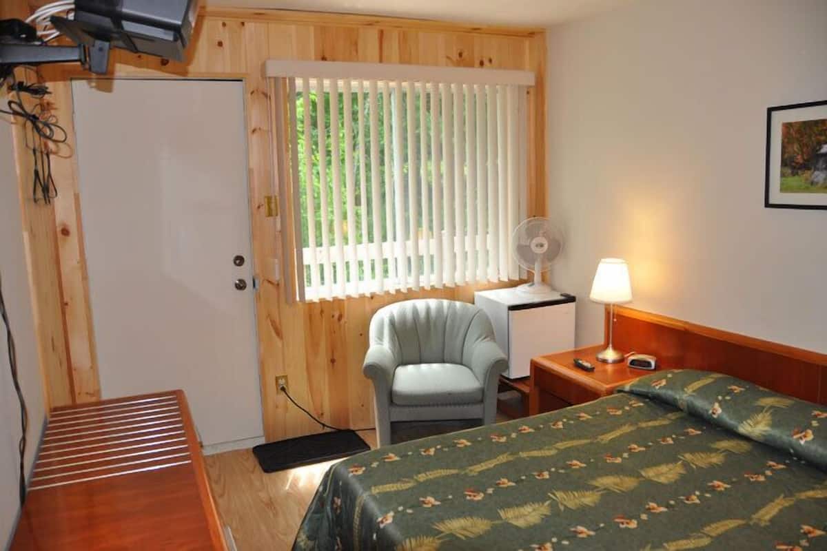 Una habitación con cama, escritorio, silla, lámpara y ventana con persianas.