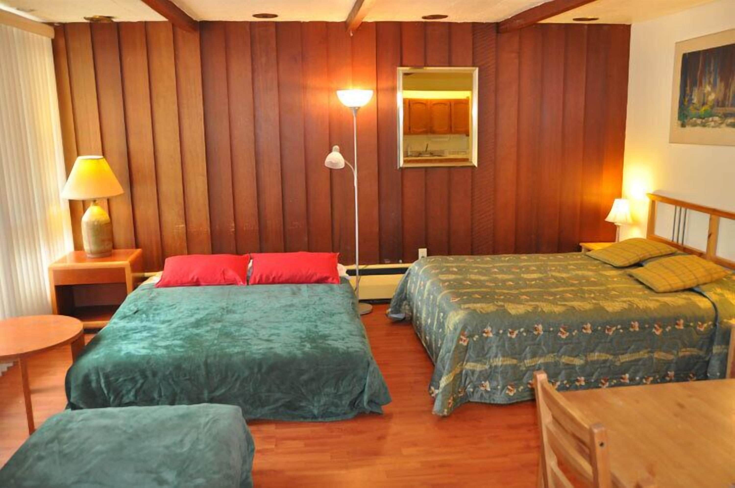 A room with two beds, wooden paneling, a mirror, and two bedside lamps.