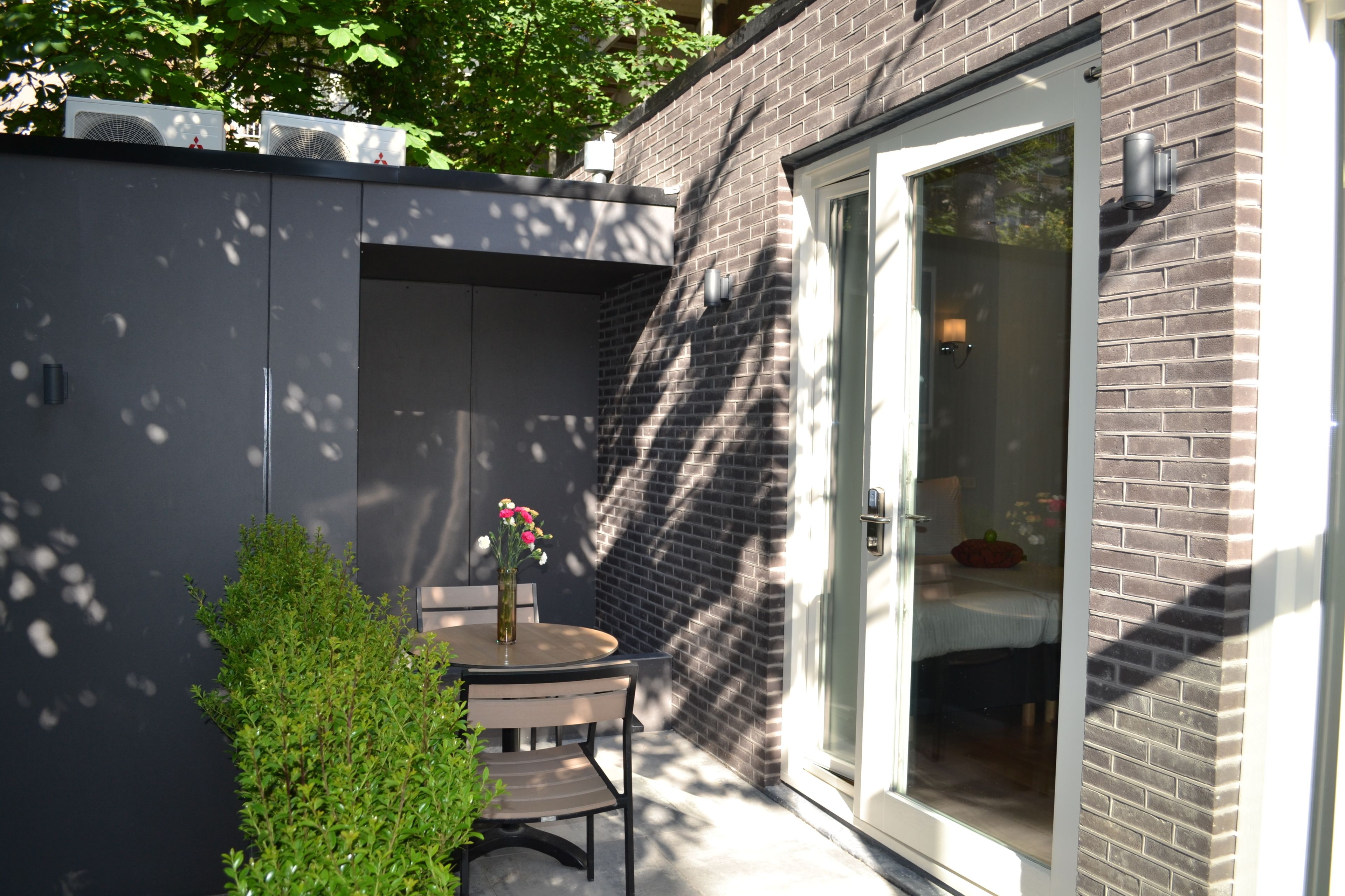 A small patio with a table and chairs, a potted plant, and a sliding glass door leading to a room.