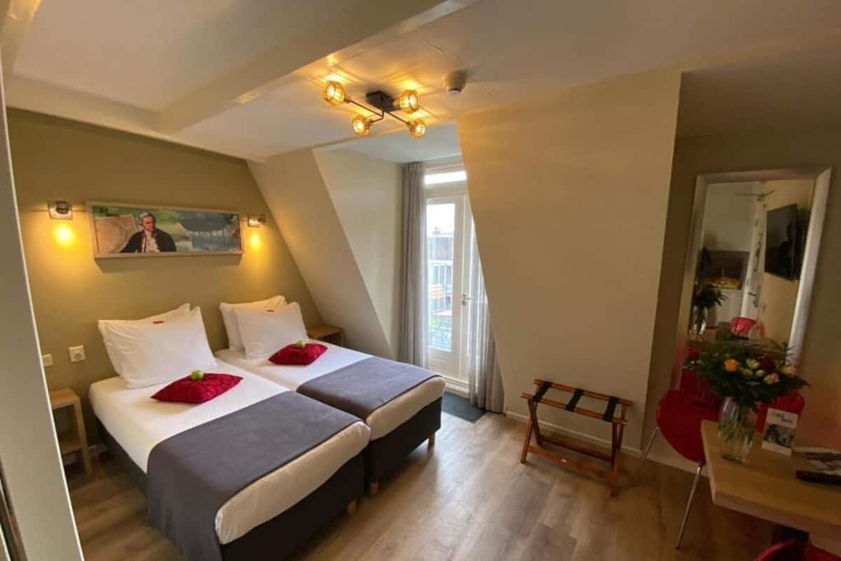 A hotel room with two beds, a desk with a chair, a mirror, and a painting on the wall.