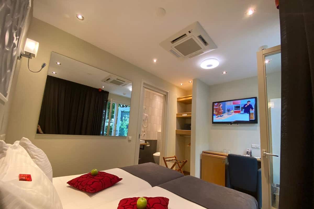 A hotel room with a bed, a TV, a mirror, and a window with curtains.