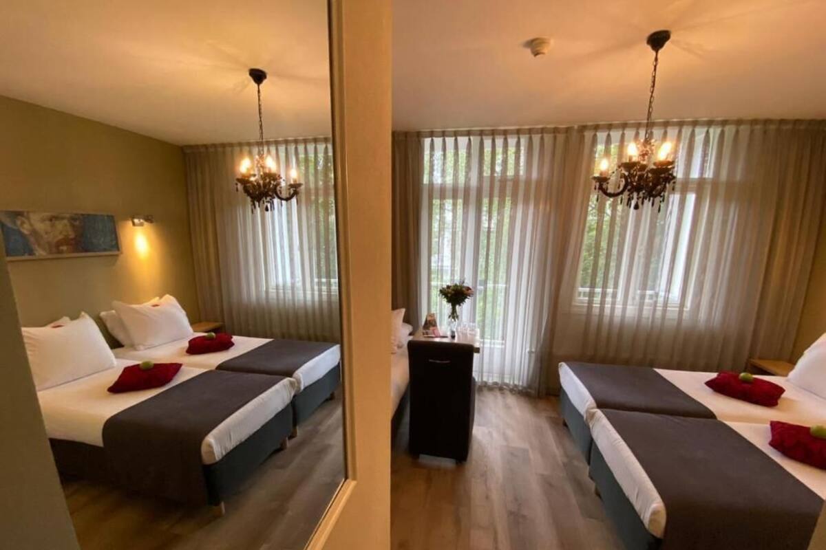 A hotel room with two beds, a desk, and a mirror.