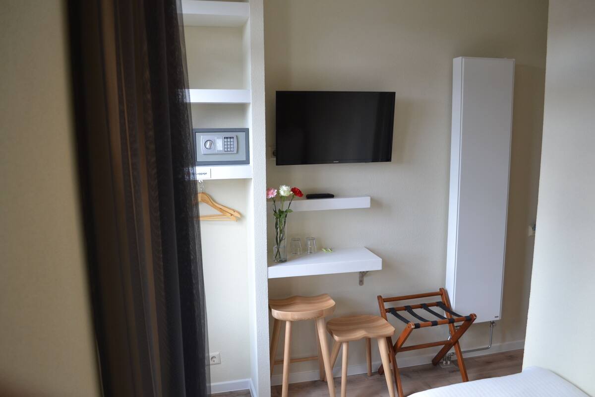A hotel room with a bed, a TV mounted on the wall, a small table with a vase of flowers, and a wooden chair.