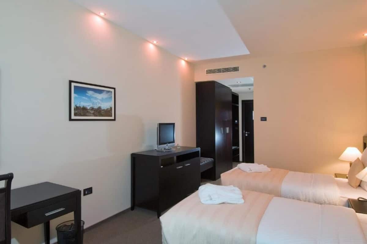 Une chambre d’hôtel avec deux lits, un bureau avec un ordinateur, une télévision et un tableau encadré au mur.