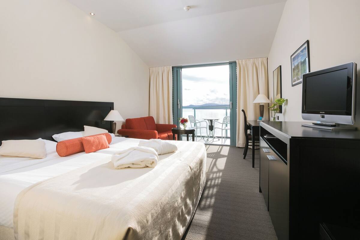 Une chambre d’hôtel avec un lit, un bureau, une télévision et une vue sur la mer.