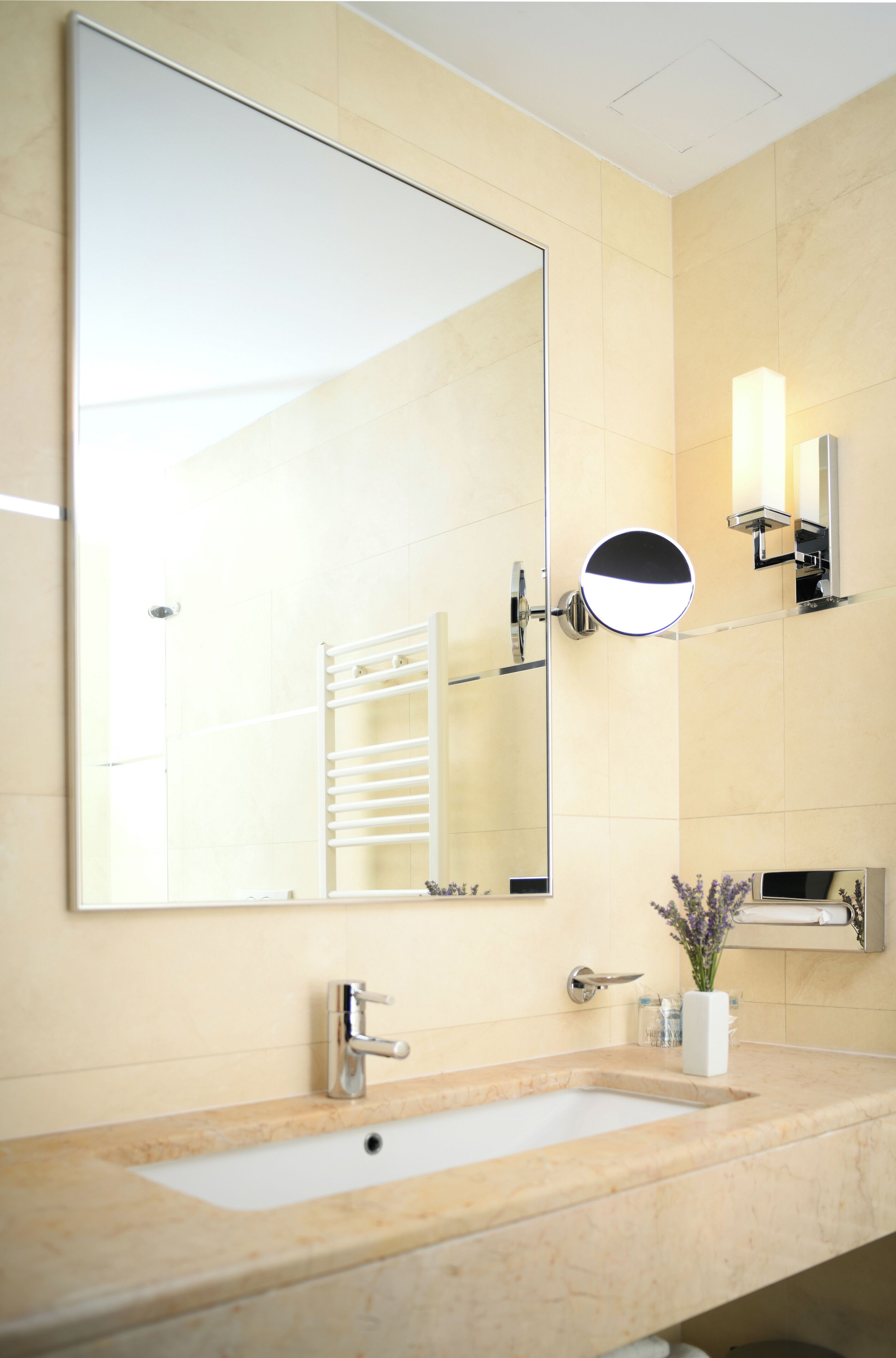 A bathroom with a large mirror, a sink, a towel rack, and a wall-mounted light fixture.