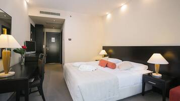 A hotel room with a bed, two bedside tables, a desk with a chair, a TV, and a mirror.