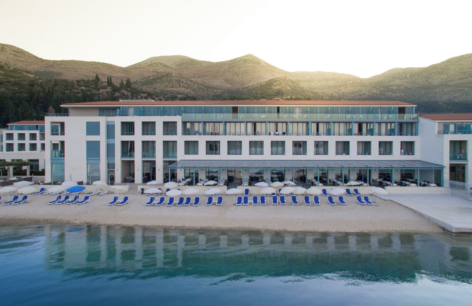 A hotel with a pool, sun loungers, and a mountain backdrop.