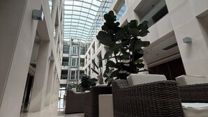 Un atrium moderne doté d’un plafond en verre, de murs blancs et d’une colonne centrale surmontée d’une grande plante.