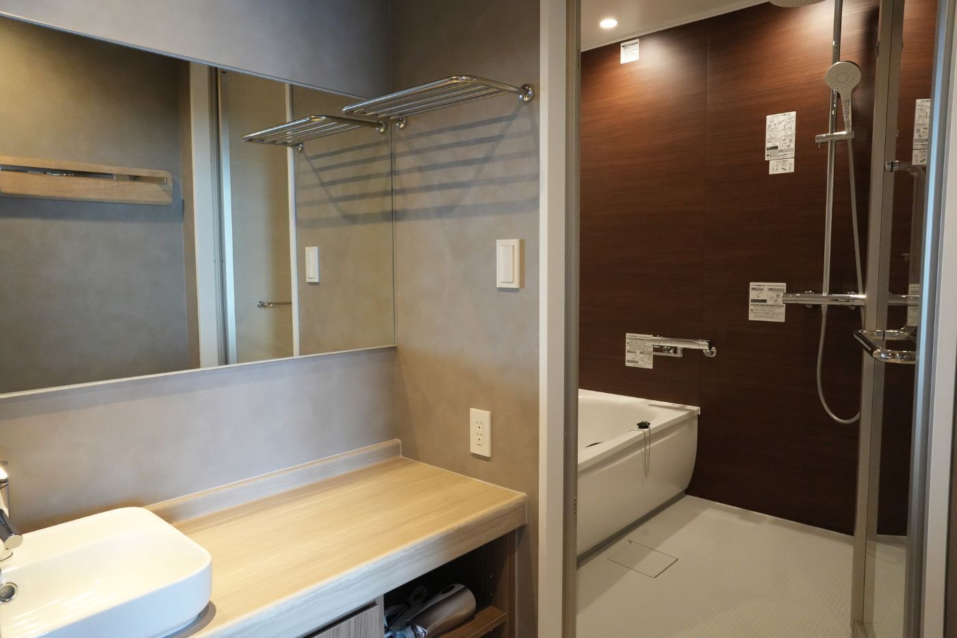 Een moderne badkamer met een grote spiegel, een wastafel, een douche en een houten opbergmeubel.