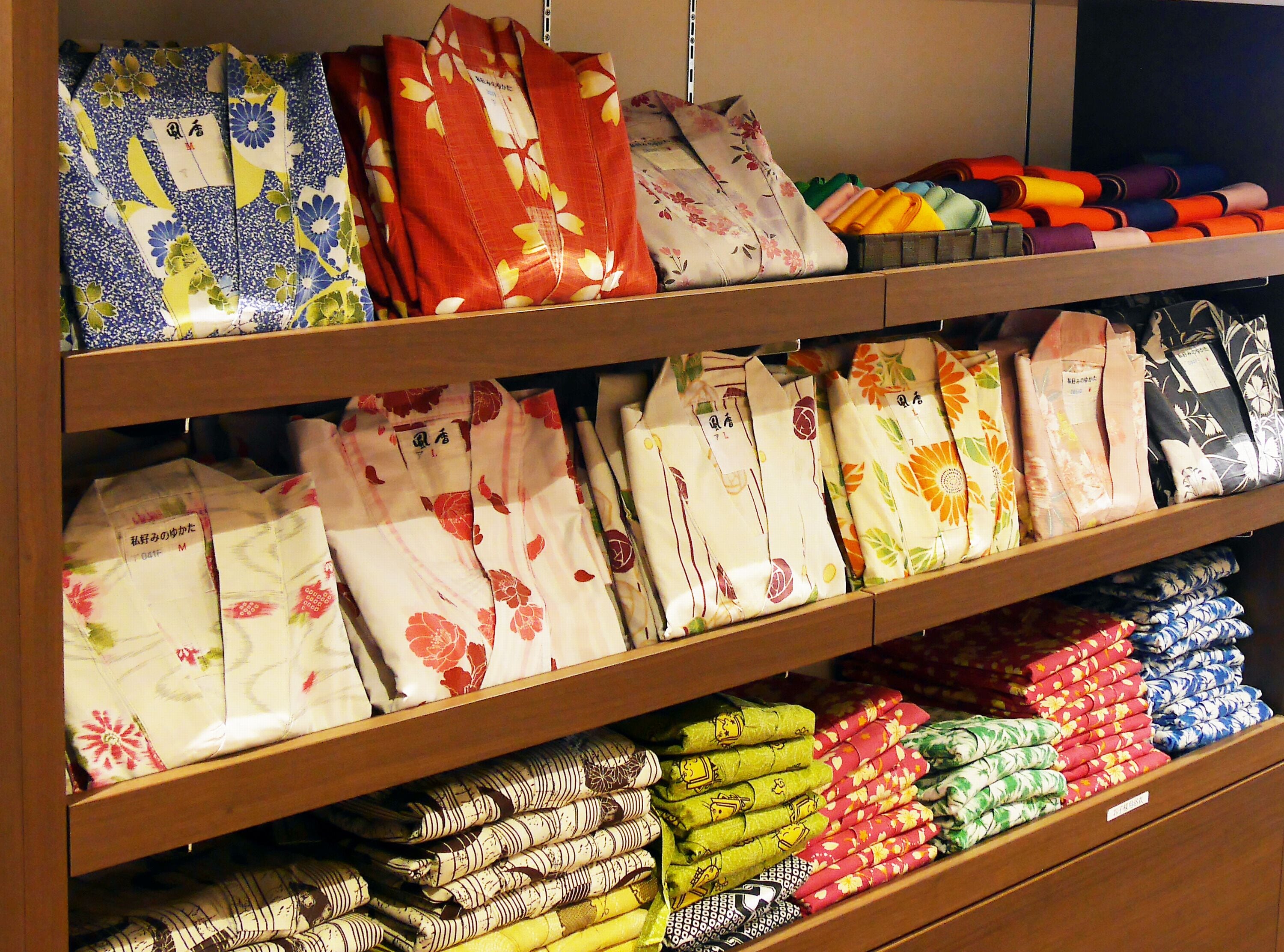 A store shelf with neatly folded fabric rolls in various patterns and colors.