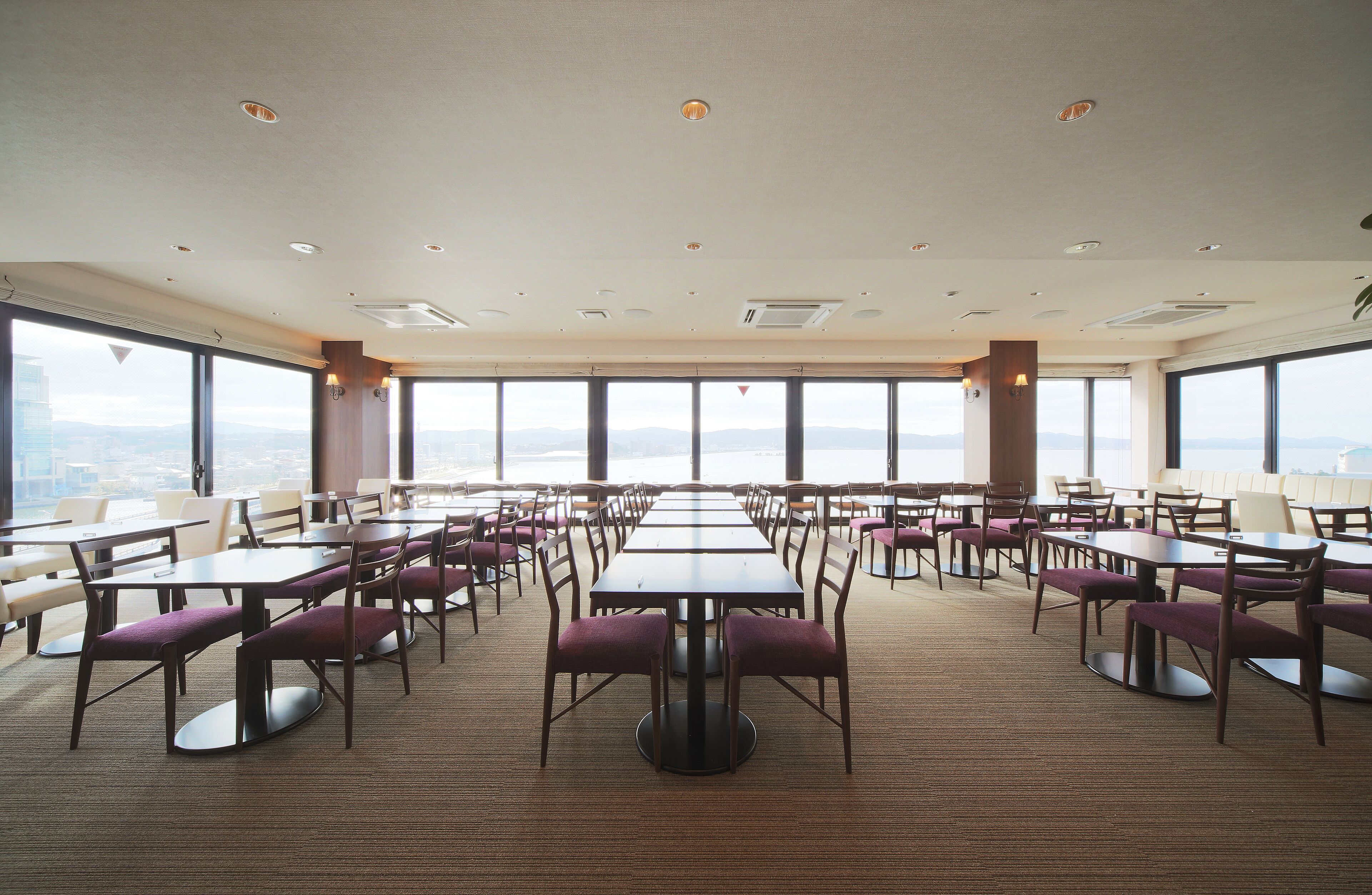 A spacious dining area with multiple tables and chairs, large windows offering a view of the cityscape.