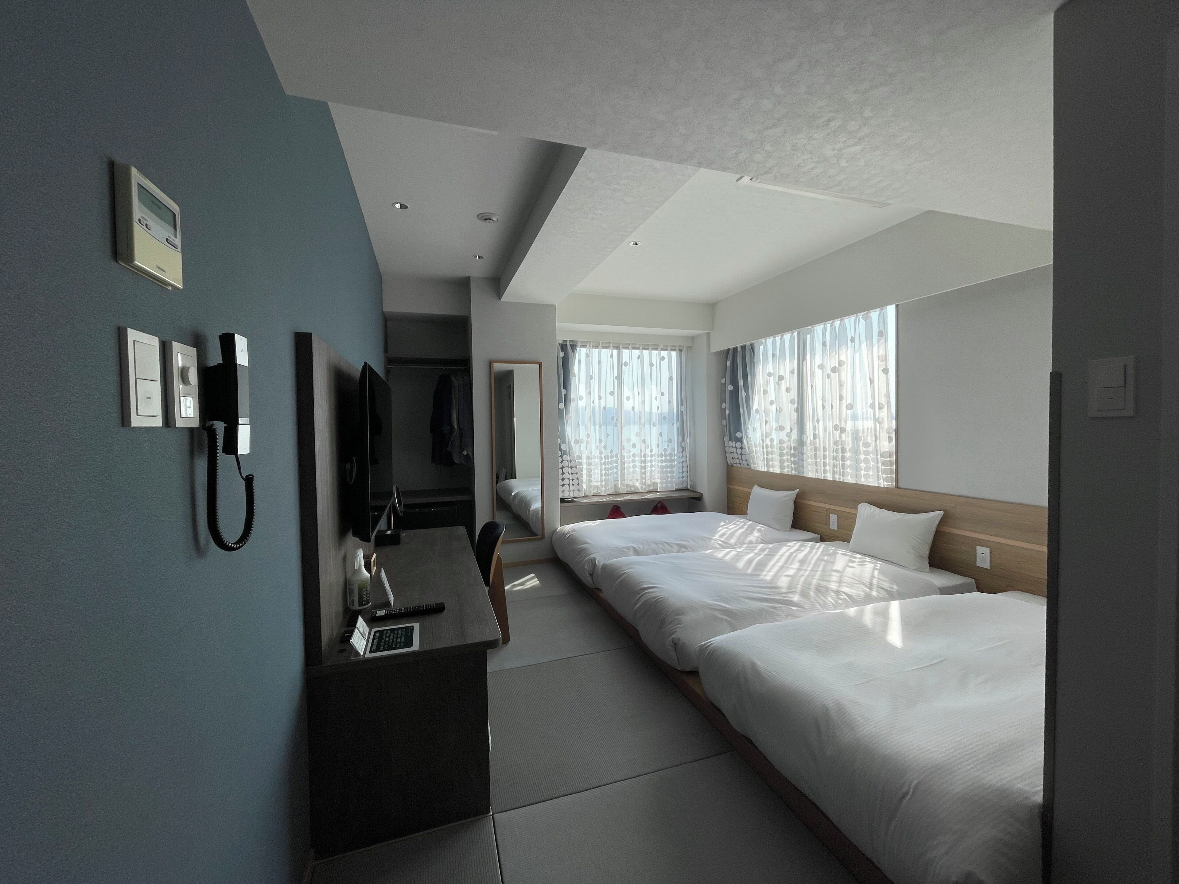 A hotel room with a desk, two beds, a mirror, and a telephone.