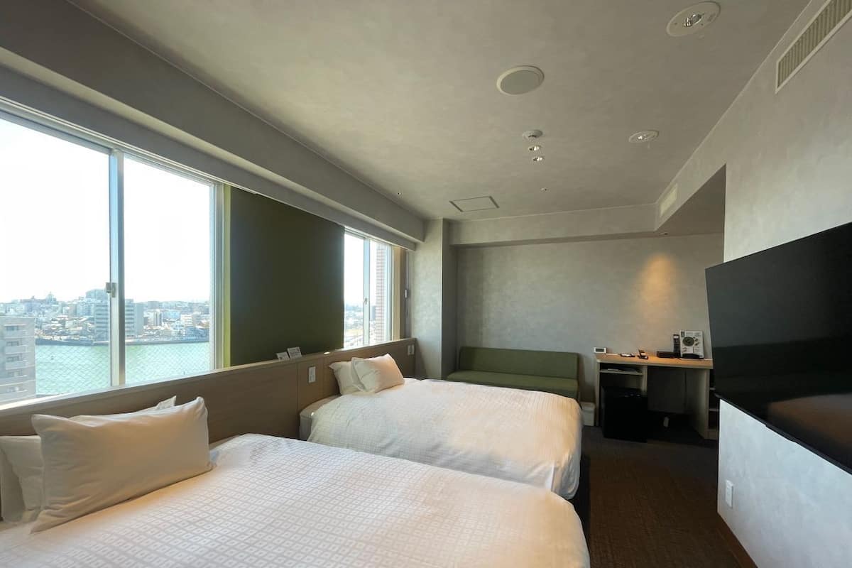 Habitación de hotel con dos camas, un escritorio, una televisión y vistas a la ciudad.
