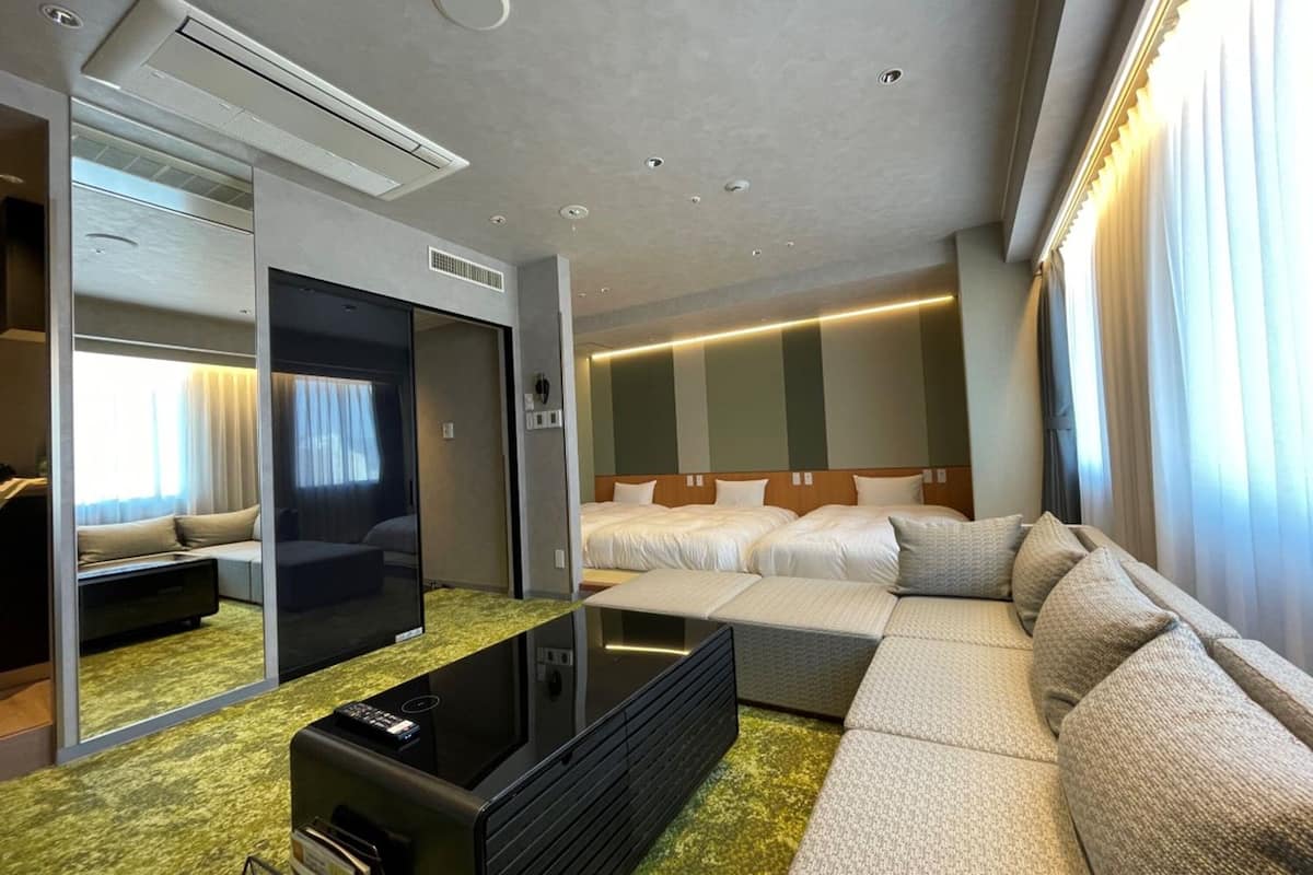 Una habitación de hotel moderna con una cama grande, un sofá, un televisor y un espejo.