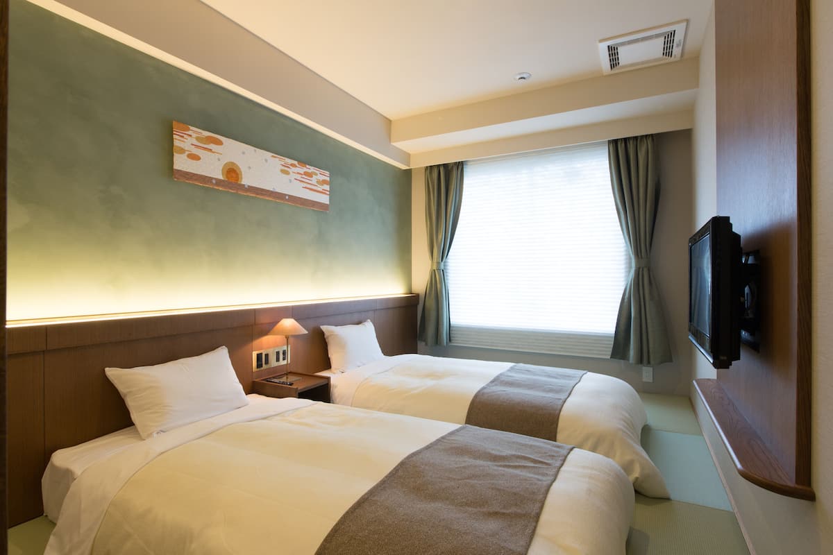 Habitación de hotel con dos camas, un televisor montado en la pared y una ventana con cortinas.
