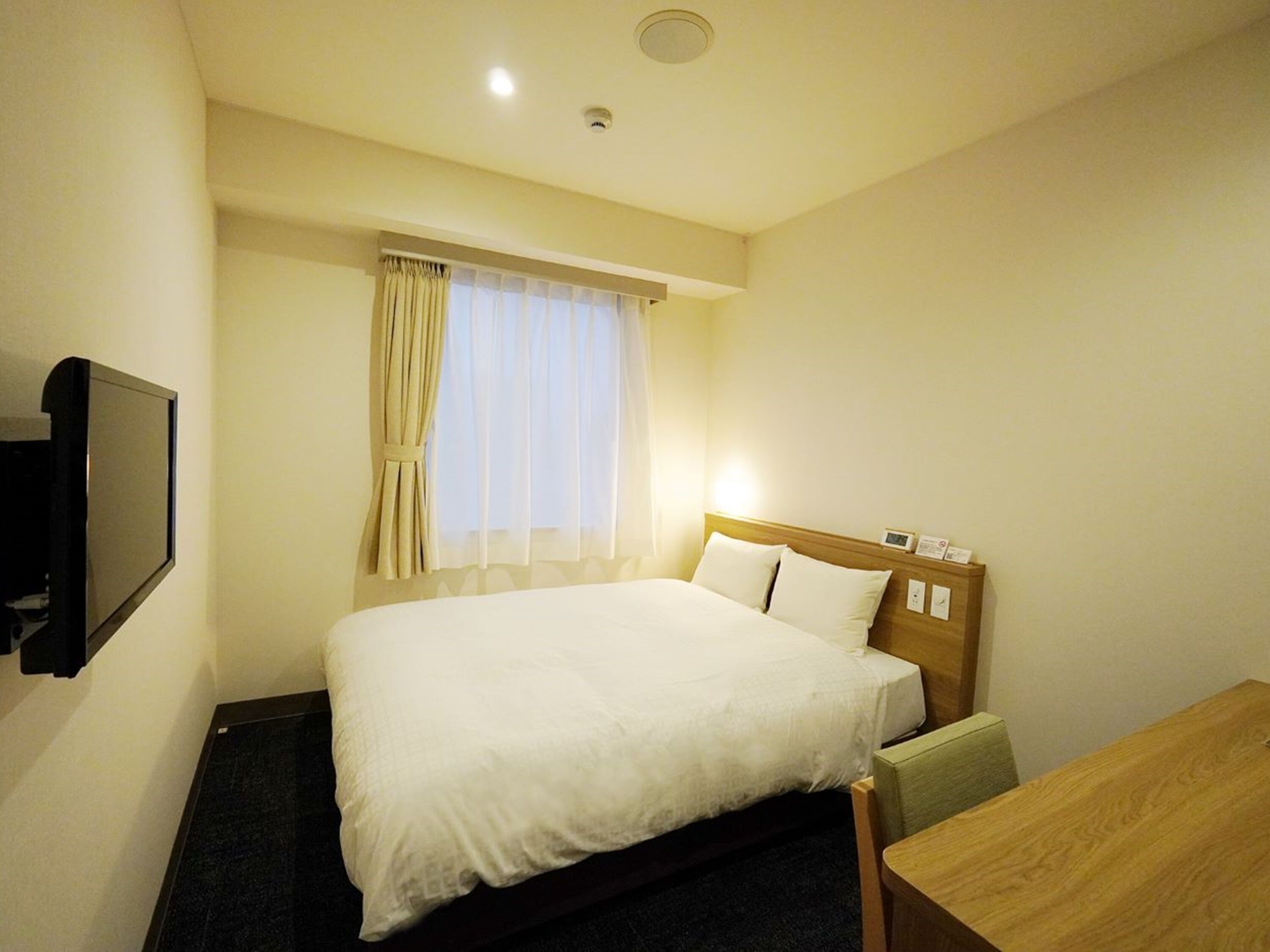 A hotel room with a bed, a desk, a television, and a window with curtains.