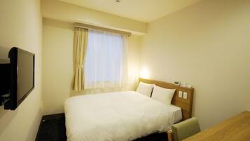 A hotel room with a bed, a desk, a television, and a window with curtains.