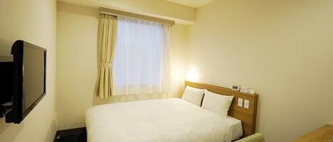 Una habitación de hotel con cama, escritorio, televisor y ventana con cortinas.