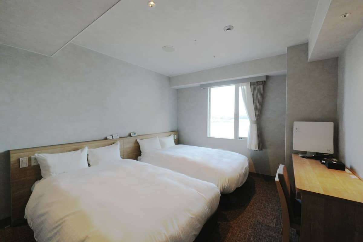 Habitación de hotel con dos camas, un escritorio con computadora y una ventana con cortinas.