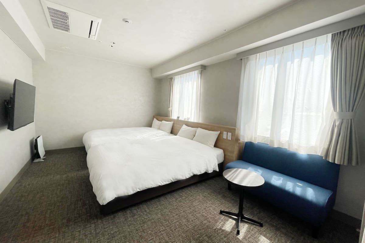 Una habitación de hotel con una cama grande, un sofá azul, una mesita redonda y un televisor en la pared.