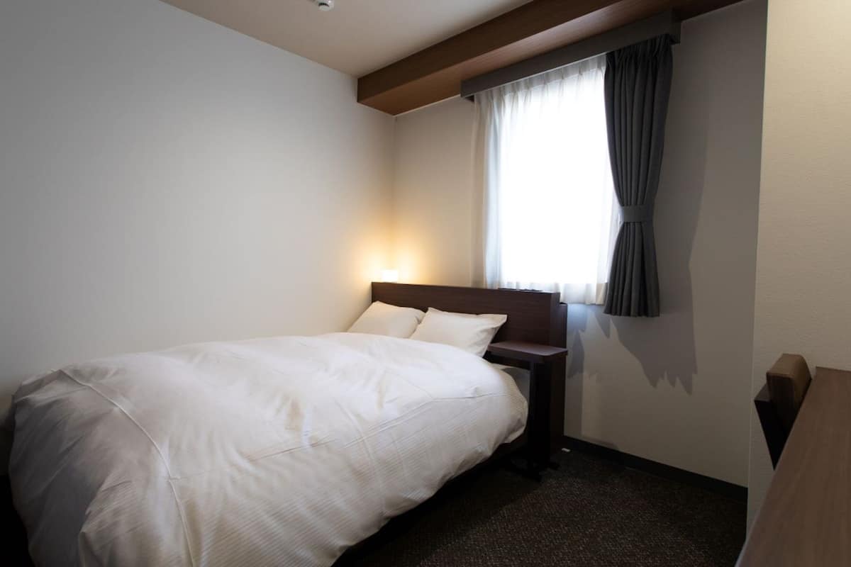 Una habitación de hotel con una cama, una mesita de noche, una ventana con cortinas y una lámpara en el techo.
