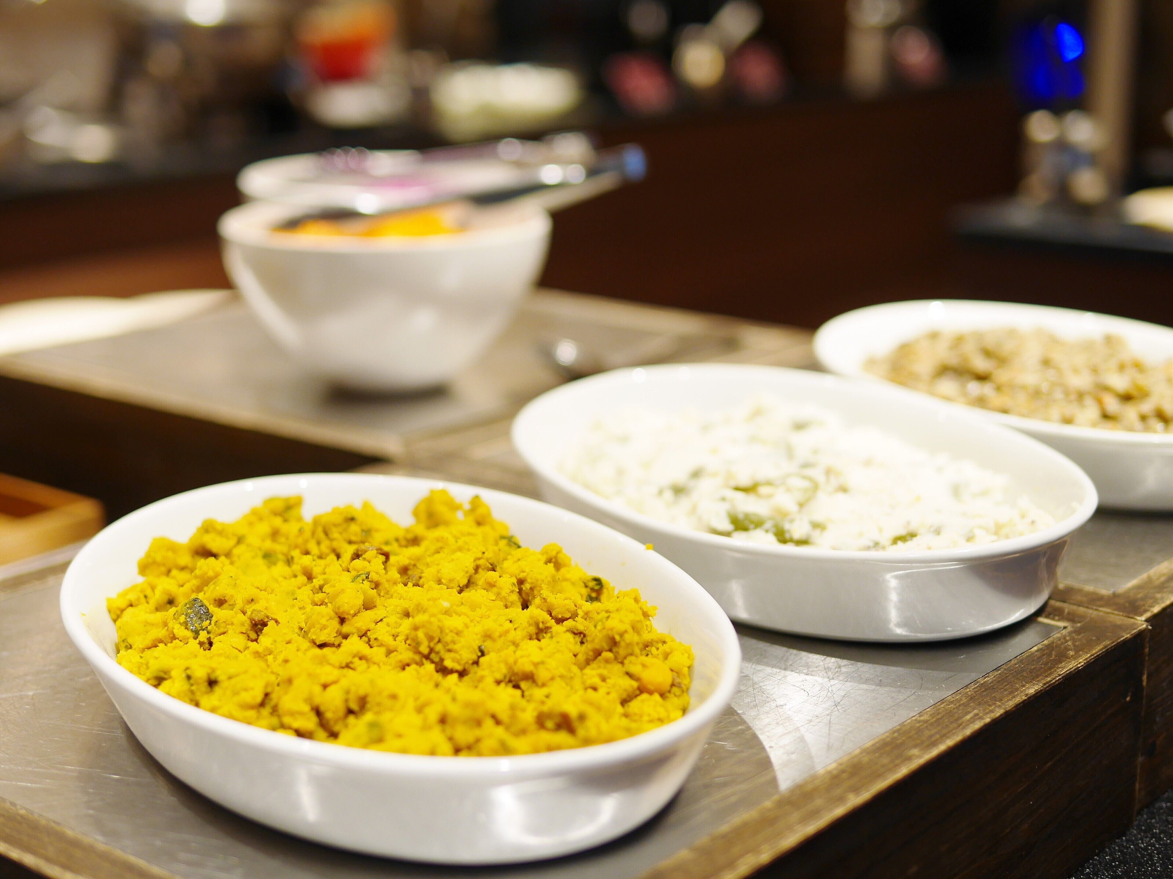 A buffet table with three white bowls containing different dishes.