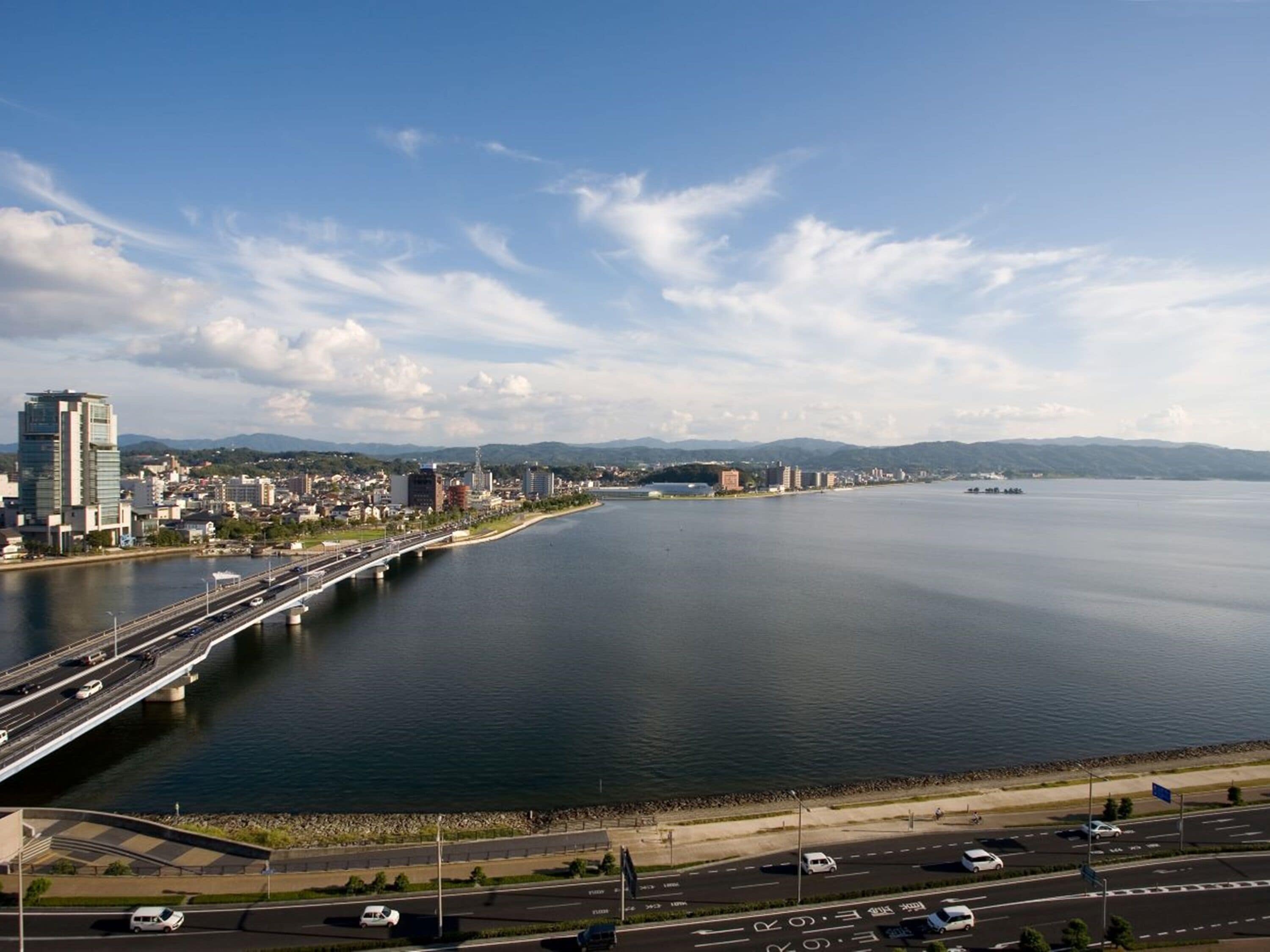 Eine Stadtlandschaft mit einem großen Gewässer, einer Brücke und einer Straße mit Fahrzeugen.