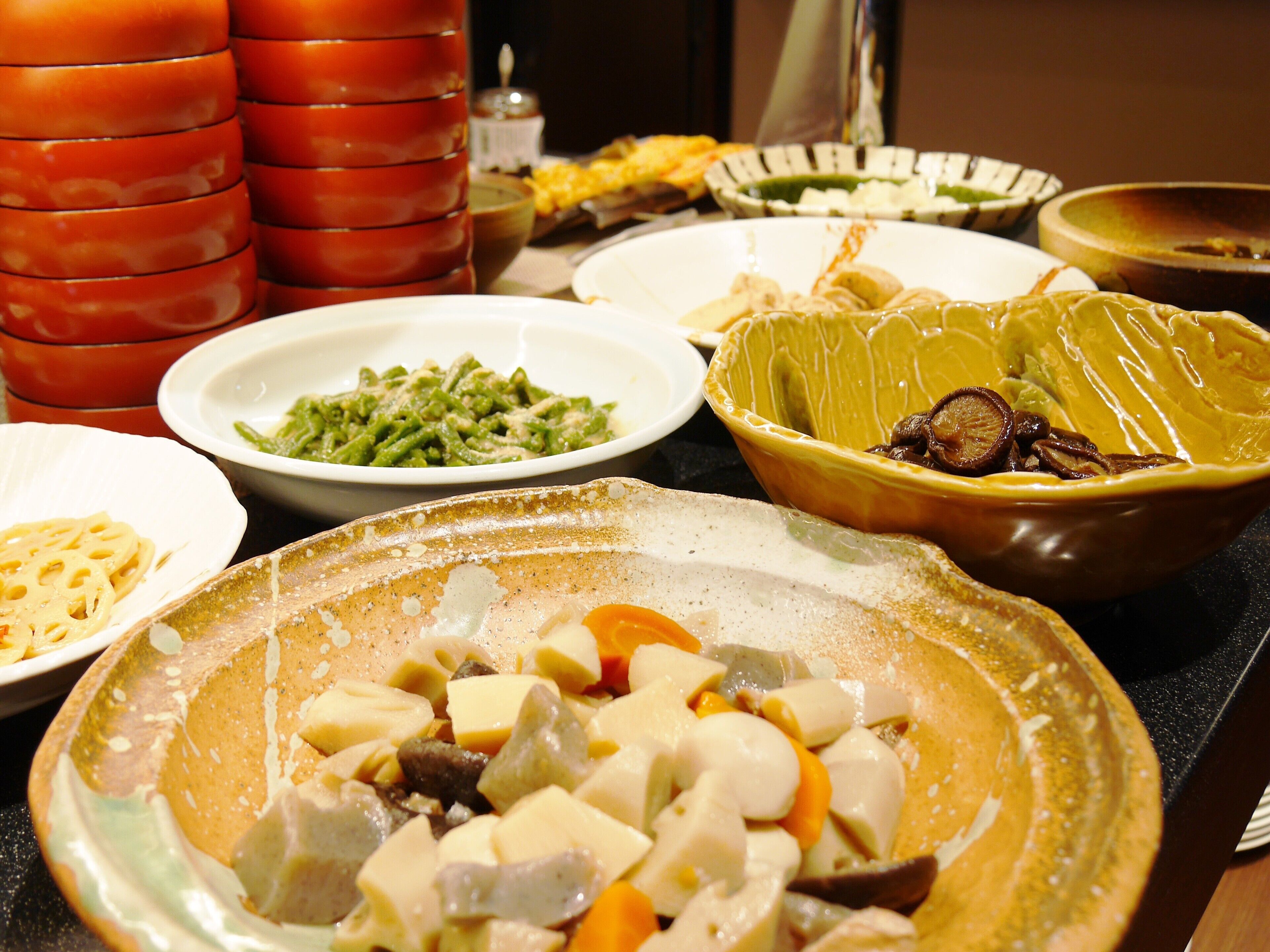 Variedad de platos en una mesa, incluyendo un tazón de vegetales cortados, un plato de pasta y varios otros platos en diferentes recipientes.