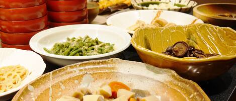 Variedad de platos en una mesa, incluyendo un tazón de vegetales cortados, un plato de pasta y varios otros platos en diferentes recipientes.