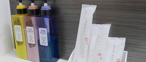 Un baño con un lavamanos blanco, tres botellas de champú, acondicionador y jabón de cuerpo, y un juego de maquinillas de afeitar y cepillos de pelo.