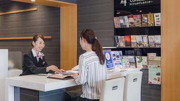A reception desk with a concierge service sign, a seating area, and a bookshelf with travel brochures.