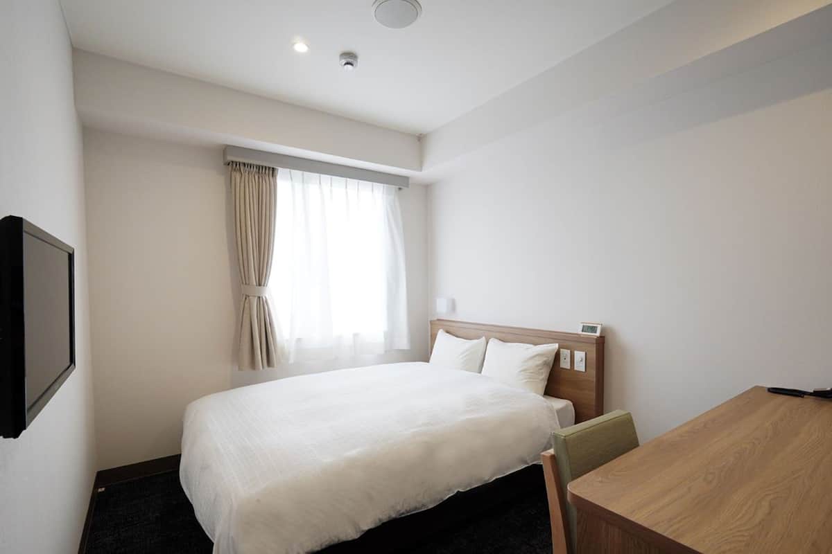 Habitación de hotel con cama, escritorio, televisor y ventana con cortinas.