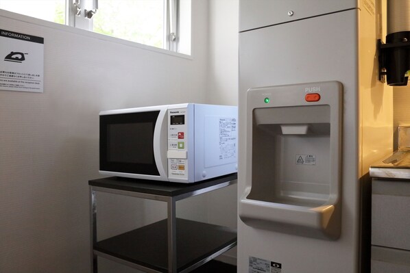 A microwave on a small table, a refrigerator with a water dispenser, and a sign with information on the wall.
