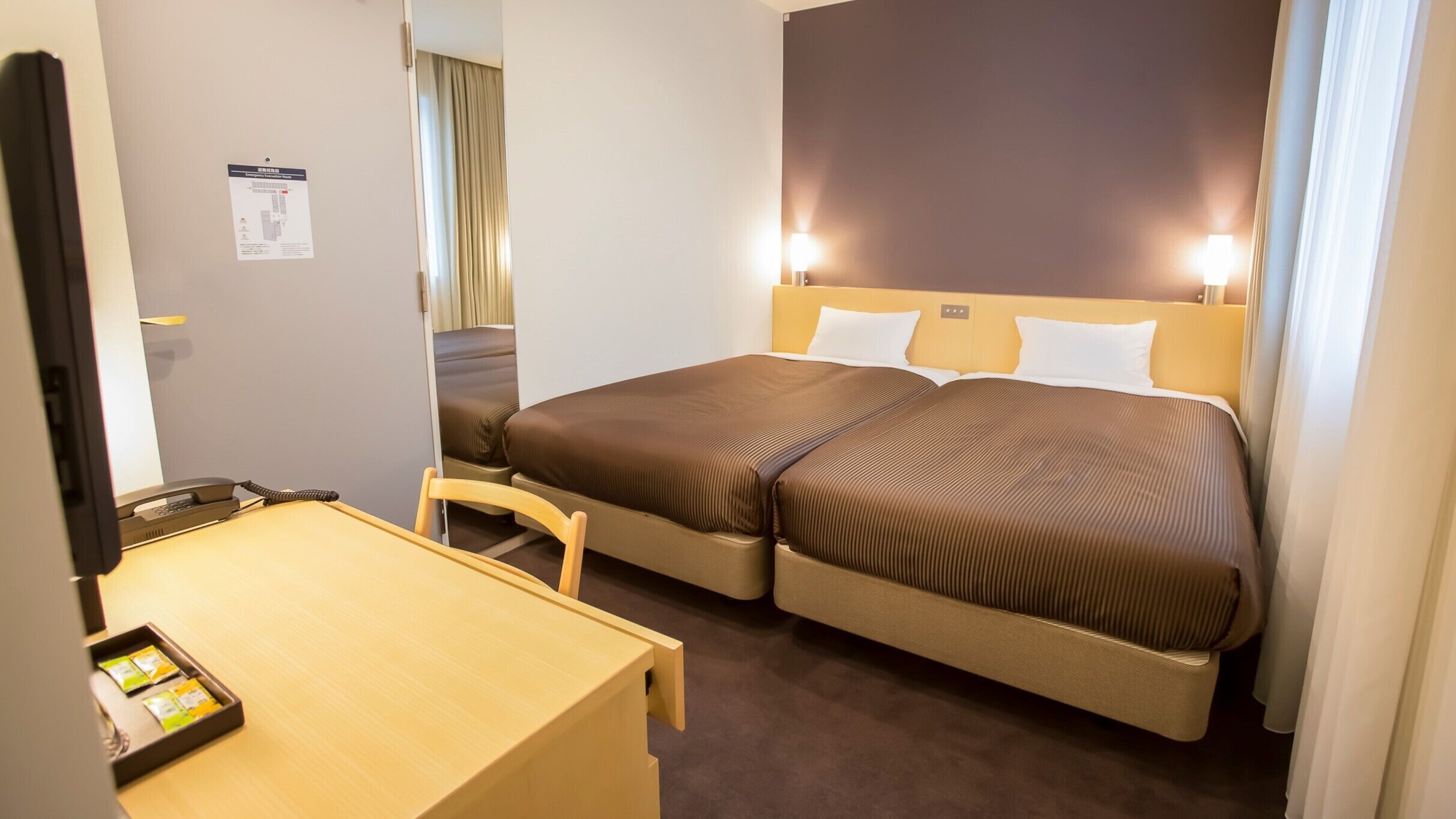 A hotel room with a bed, a desk, a chair, and a telephone.