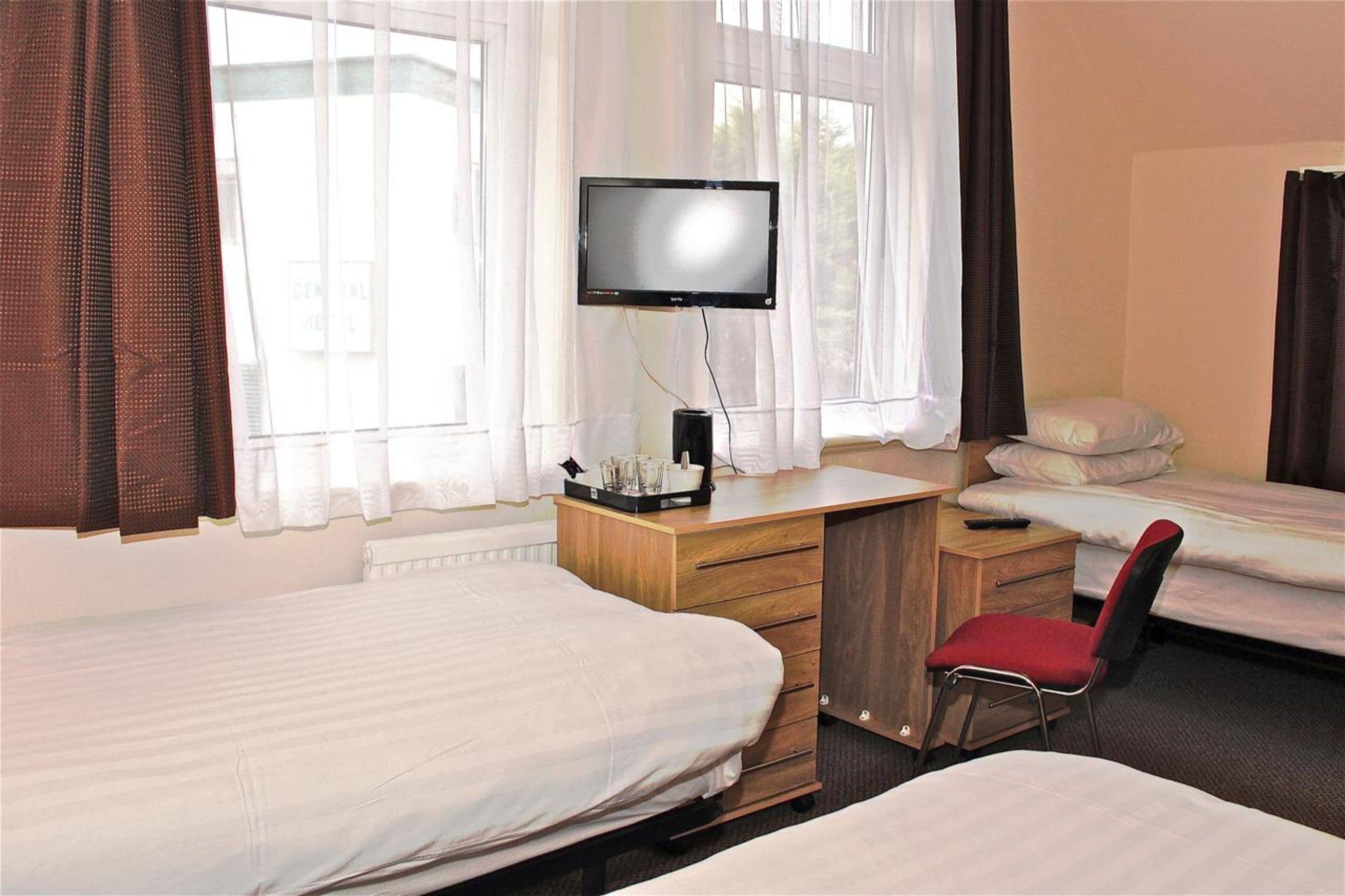 A hotel room with two beds, a desk with a television, and a chair.