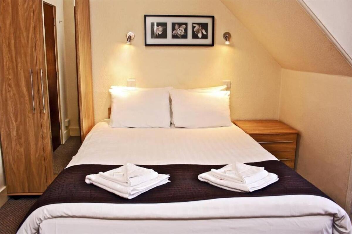 A hotel room with a bed, two pillows, a nightstand, a wooden wardrobe, and a framed picture on the wall.