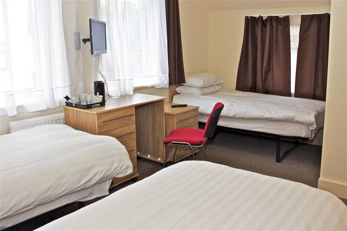 A hotel room with two single beds, a desk with a chair, a television, and a window with curtains.