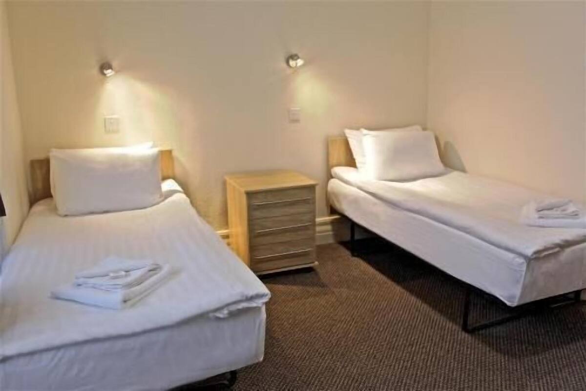 A room with two single beds, a wooden nightstand, and a carpeted floor.