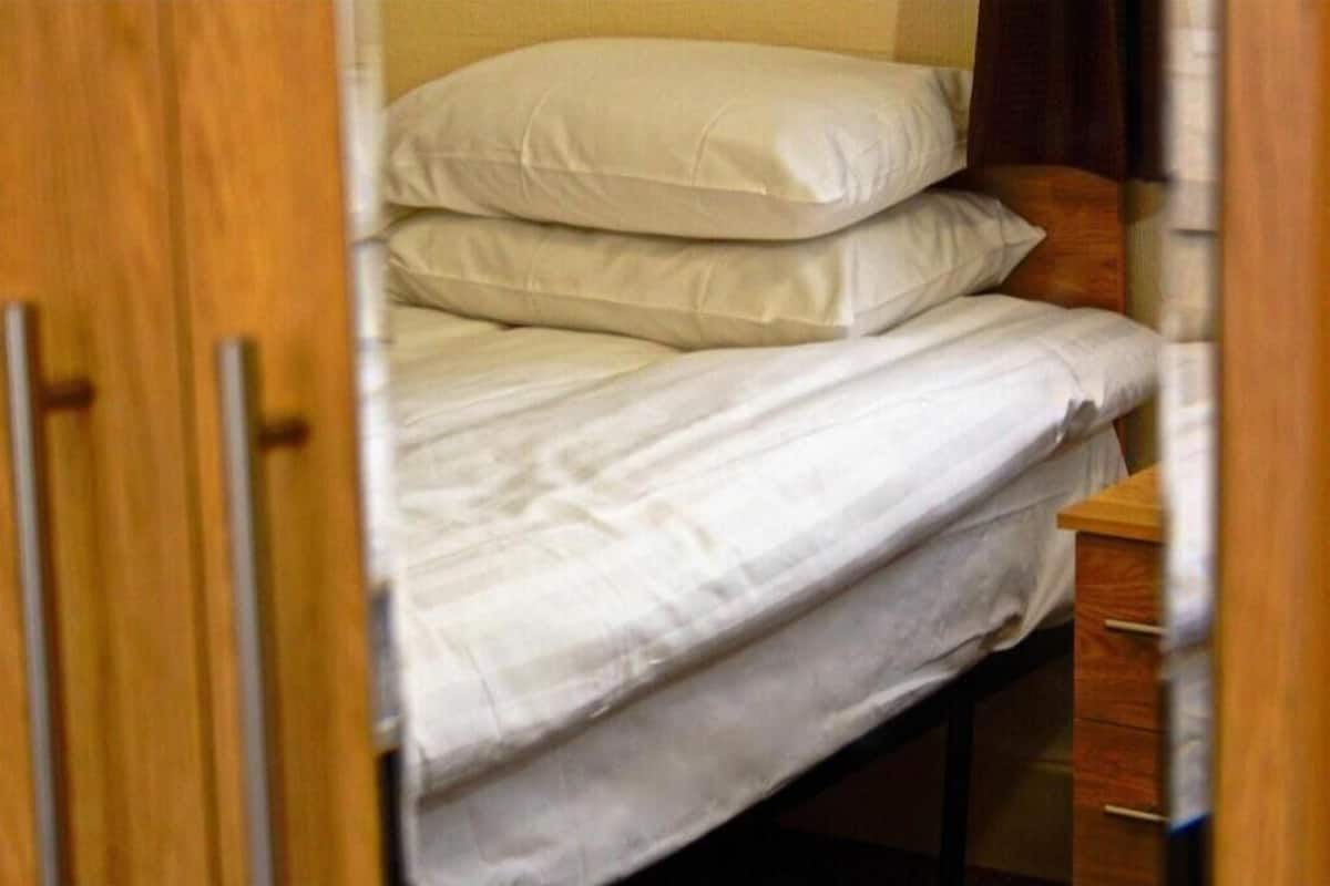 A bed with white bedding, a wooden headboard, and a wooden nightstand with drawers.